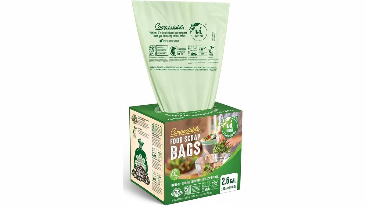 Compostable bags beside a small stainless steel kitchen compost bin on a countertop