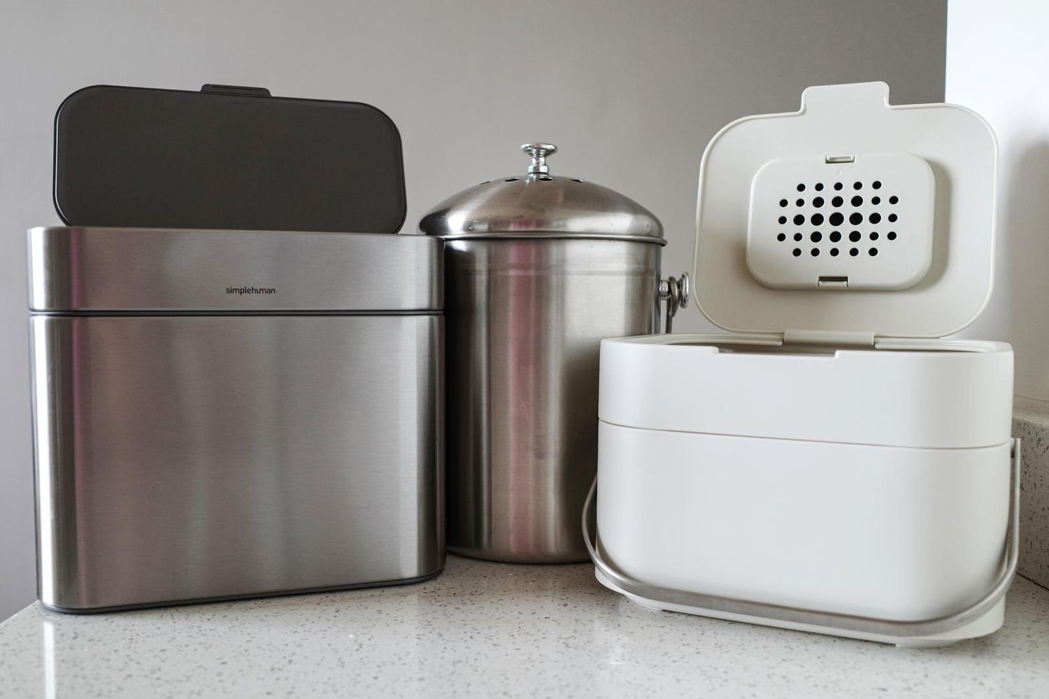 Stainless steel compost pail on a bright kitchen countertop with vegetable scraps nearby
