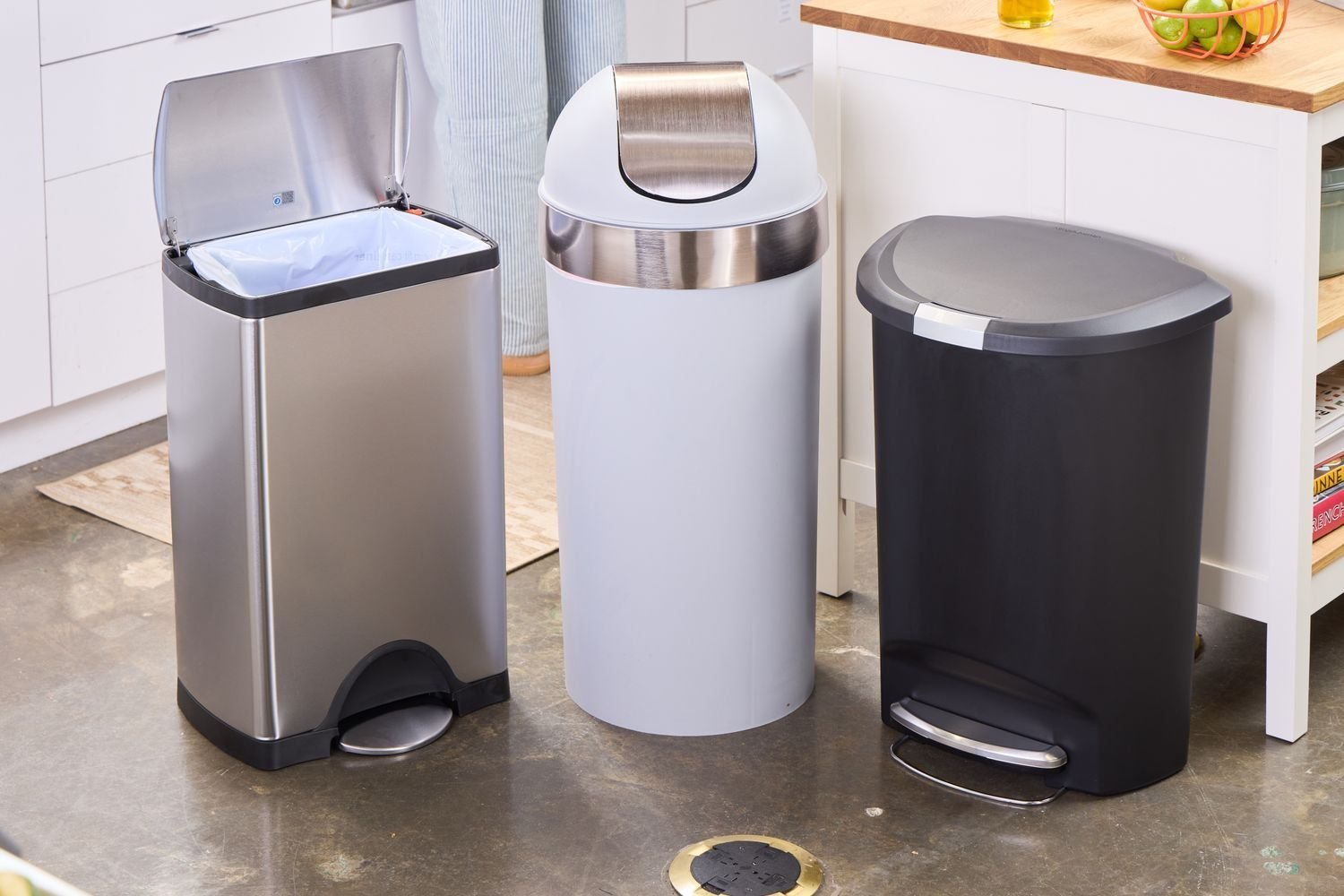 A stainless steel kitchen waste bin standing on a wooden floor in a bright modern kitchen